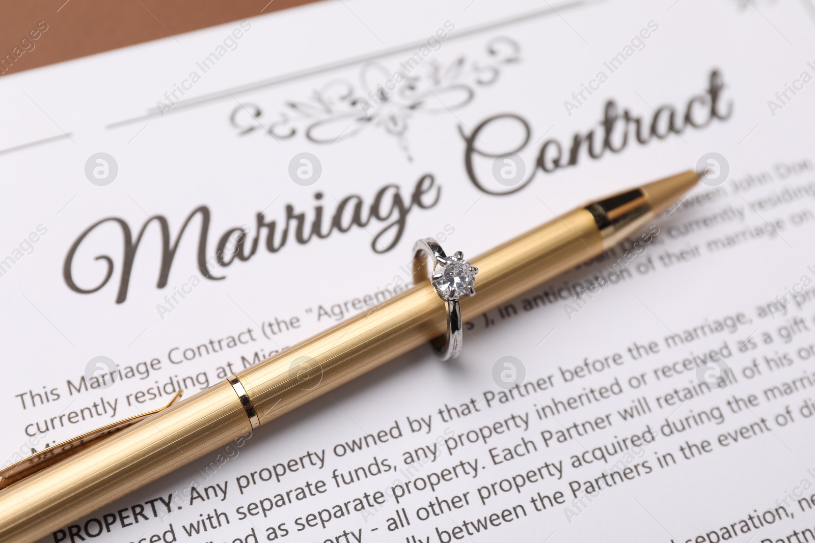 Photo of Marriage contract and pen with ring on brown background, closeup