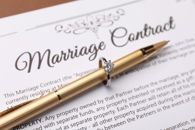 Photo of Marriage contract and pen with ring on brown background, closeup