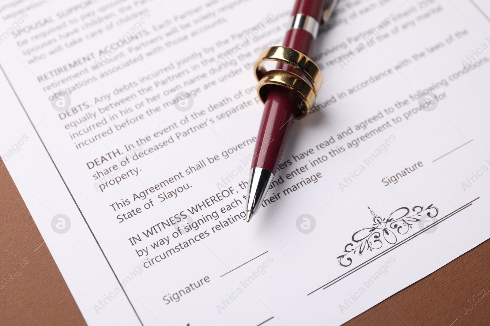 Photo of Marriage contract, pen and golden rings on brown background, closeup