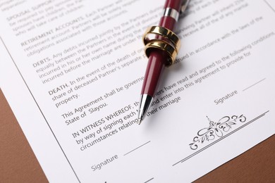 Photo of Marriage contract, pen and golden rings on brown background, closeup