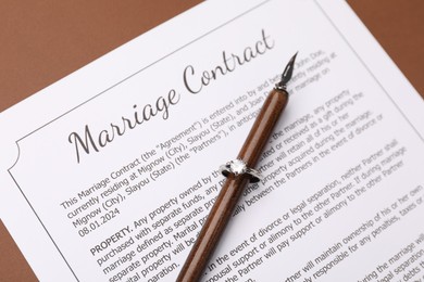 Photo of Marriage contract, pen and ring on brown background, above view