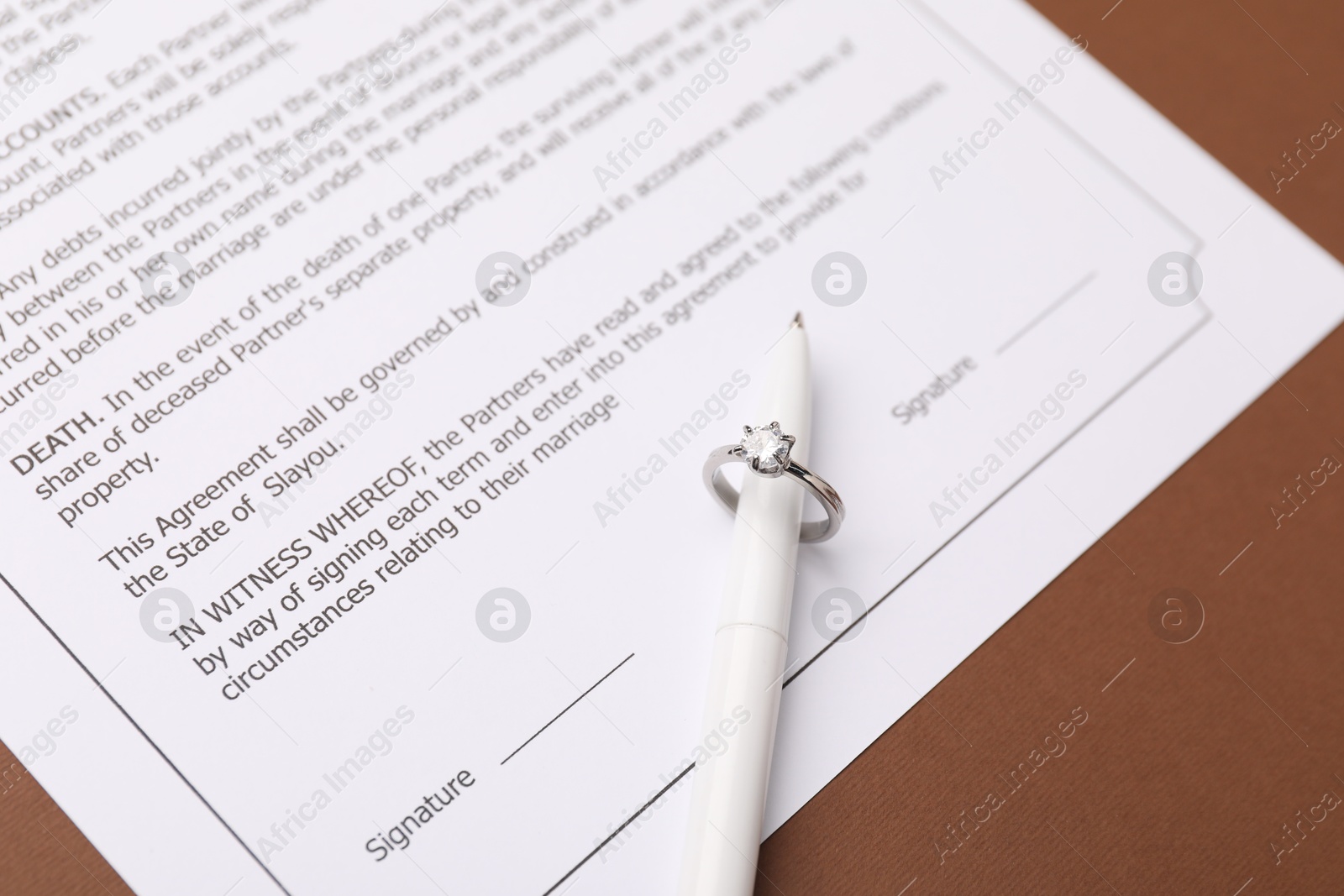 Photo of Marriage contract, pen and ring on brown background, closeup