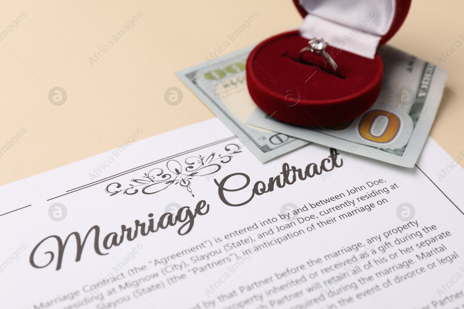 Photo of Marriage contract, dollar bill and ring on beige table, closeup