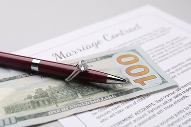 Photo of Marriage contract, pen with ring and dollar bill on grey table, closeup