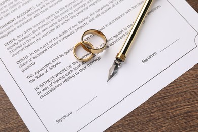 Photo of Marriage contract, pen and golden rings on wooden table, top view