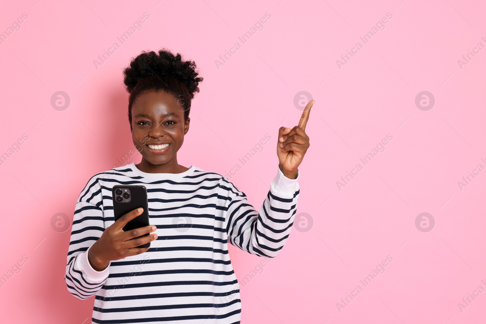 Photo of Cheerful woman with smartphone pointing at something on pink background. Space for text