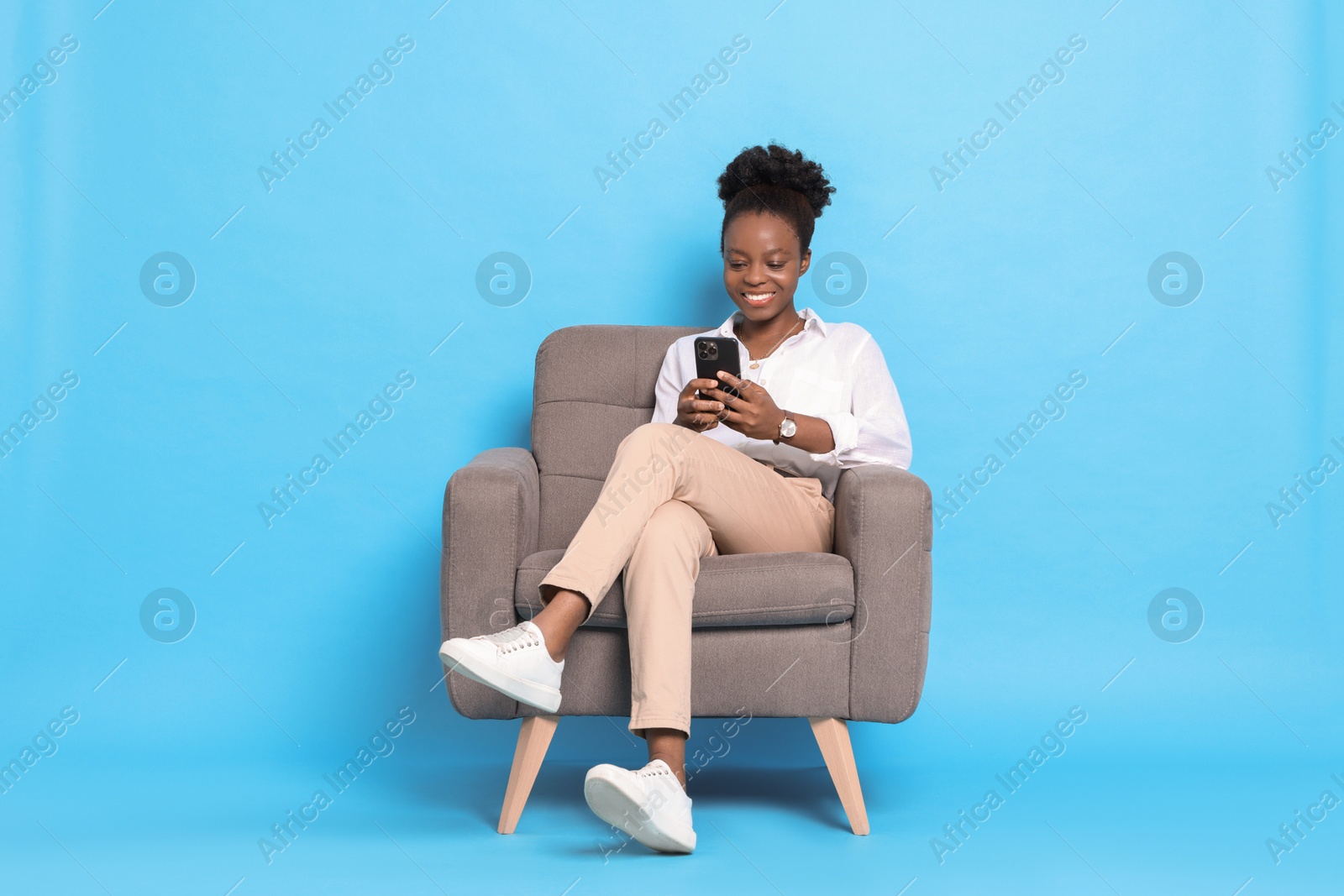 Photo of Smiling woman with smartphone sitting in armchair on light blue background