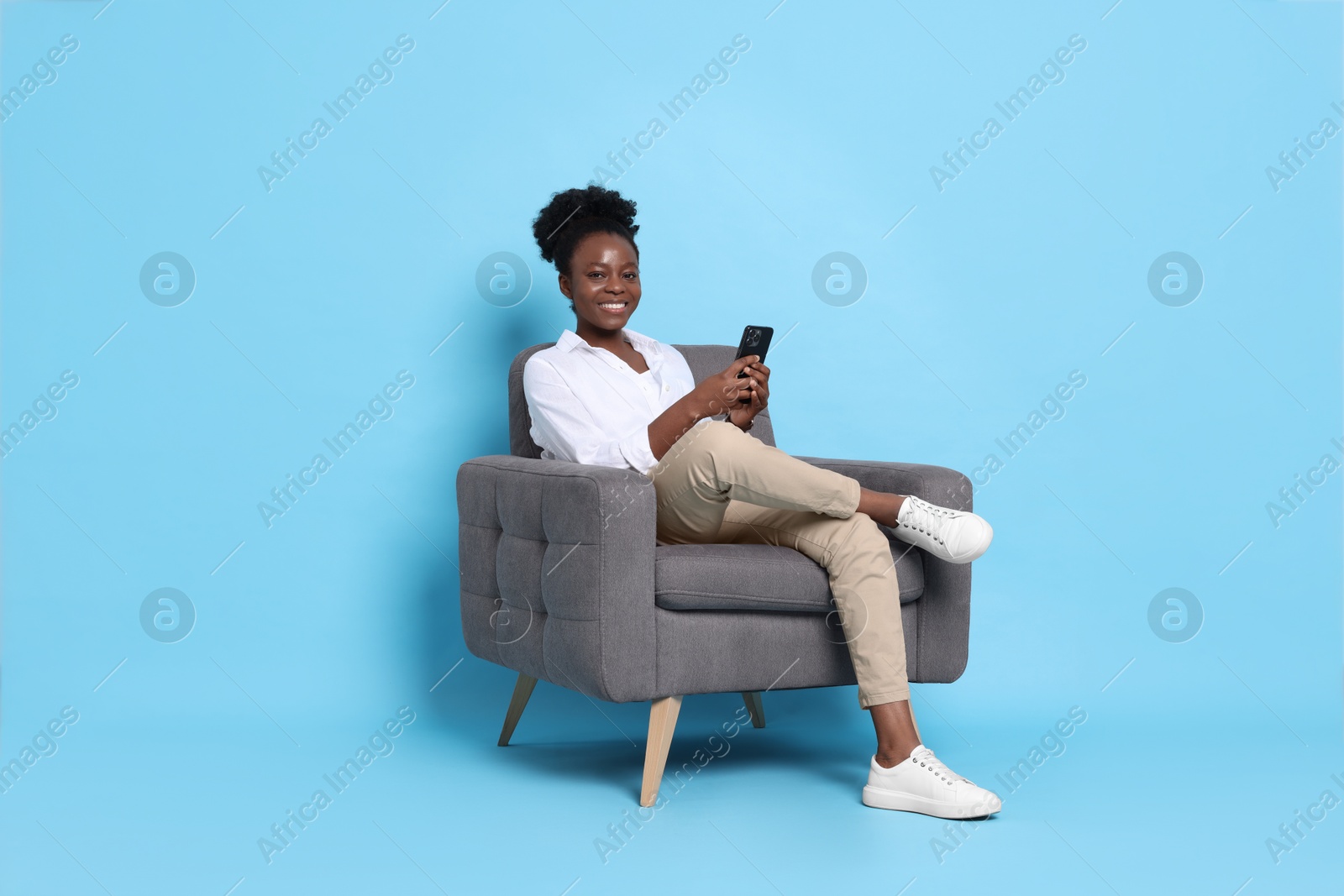 Photo of Smiling woman with smartphone sitting in armchair on light blue background