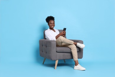 Photo of Smiling woman with smartphone sitting in armchair on light blue background