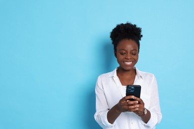 Happy woman with smartphone on light blue background. Space for text