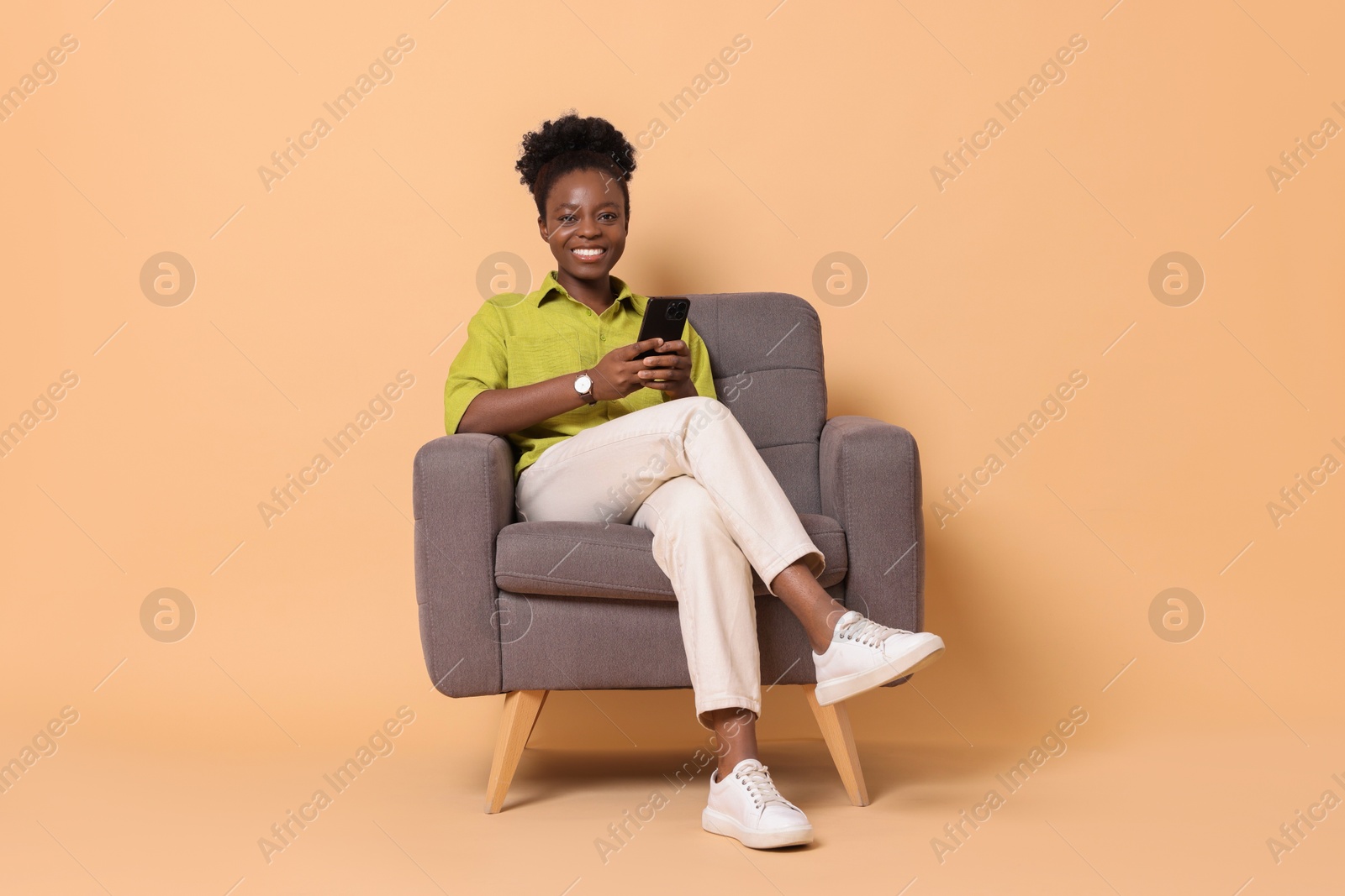 Photo of Smiling woman with smartphone sitting in armchair on beige background