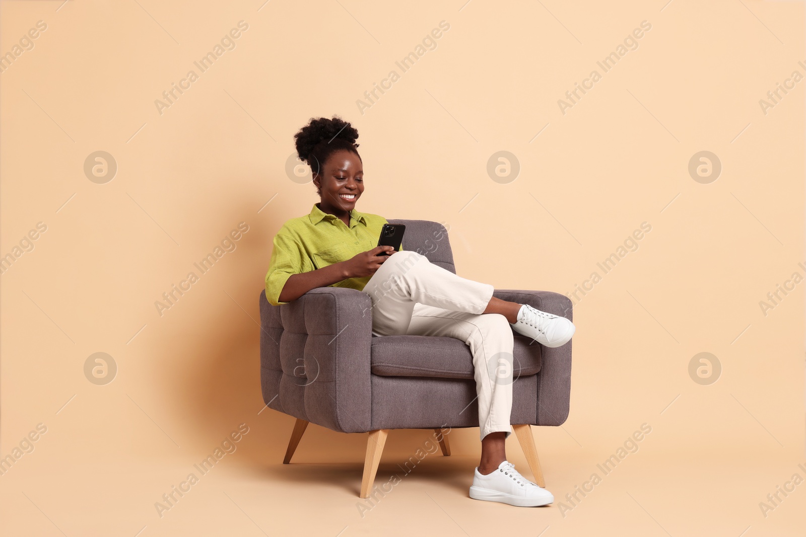 Photo of Smiling woman with smartphone sitting in armchair on beige background