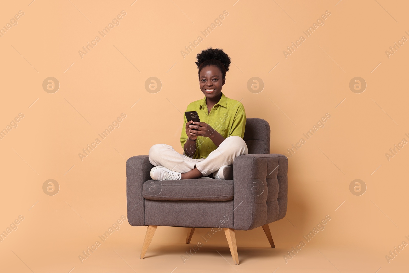 Photo of Smiling woman with smartphone sitting in armchair on beige background