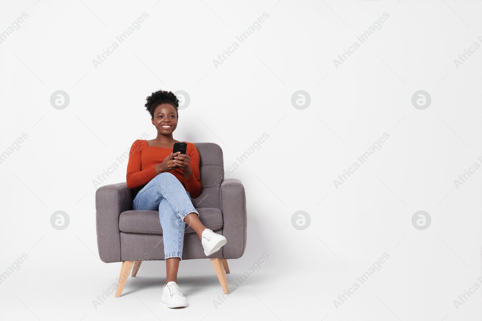 Photo of Smiling woman with smartphone sitting in armchair on white background. Space for text