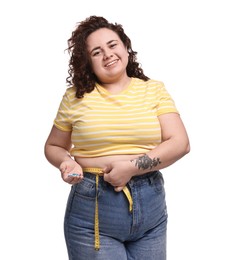 Photo of Happy plus size woman measuring waist with tape and holding pile of weight loss supplements on white background