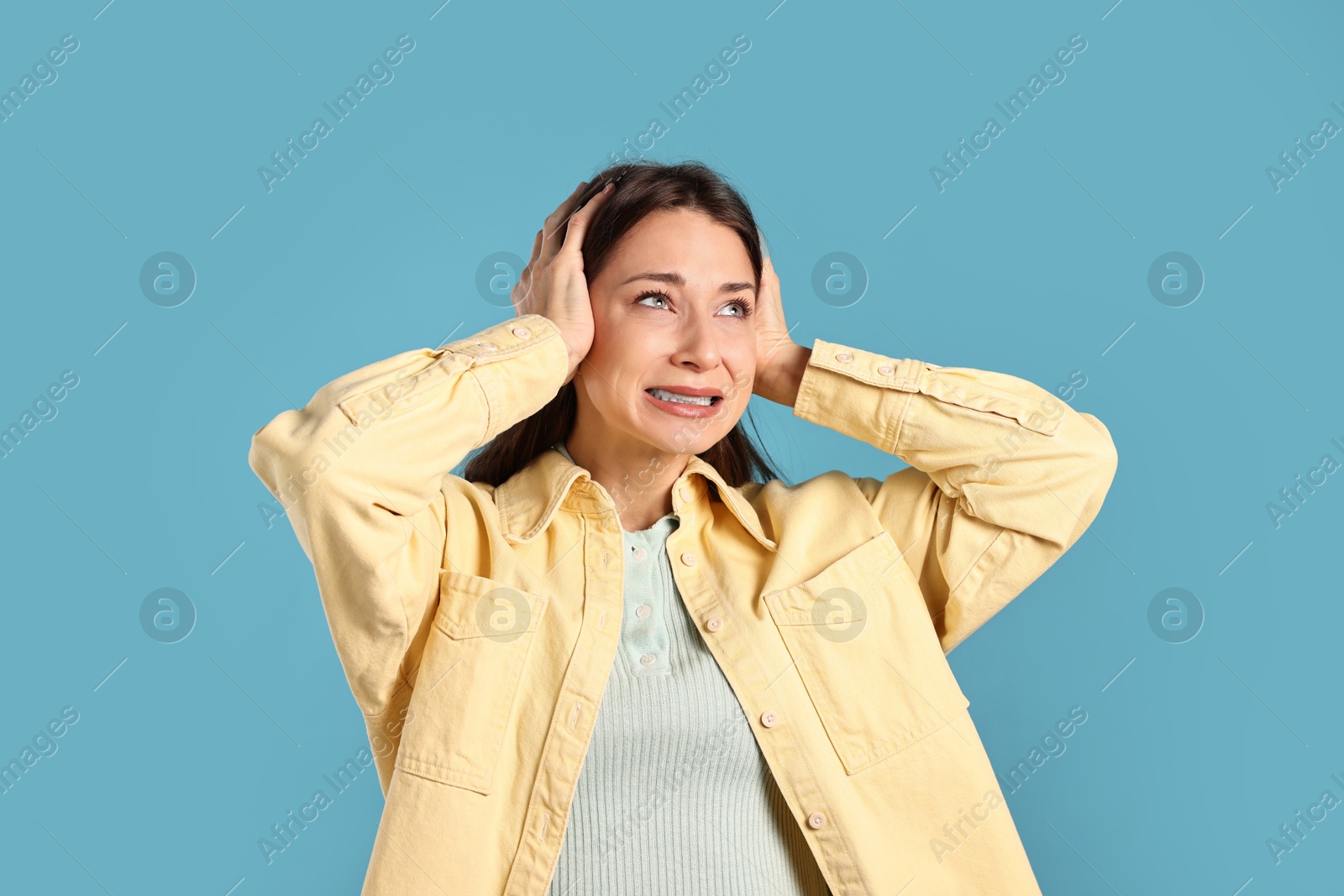 Photo of Annoyed woman covering her ears due to loud sound on light blue background