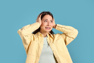 Photo of Annoyed woman covering her ears due to loud sound on light blue background