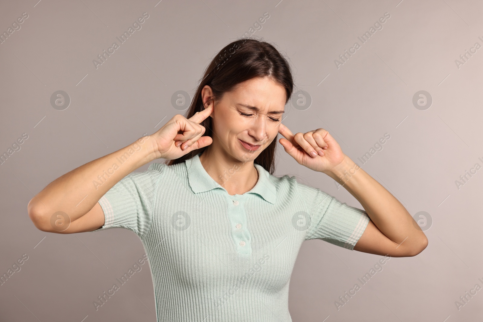 Photo of Annoyed woman covering her ears due to loud sound on light grey background