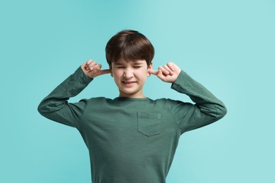 Photo of Annoyed boy covering his ears due to loud sound on light blue background