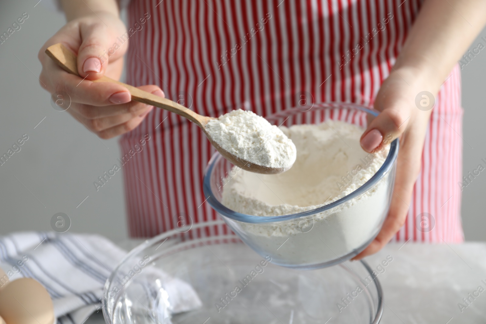 Photo of Making cinnamon rolls. Woman adding flour into bowl at gray marble table, closeup