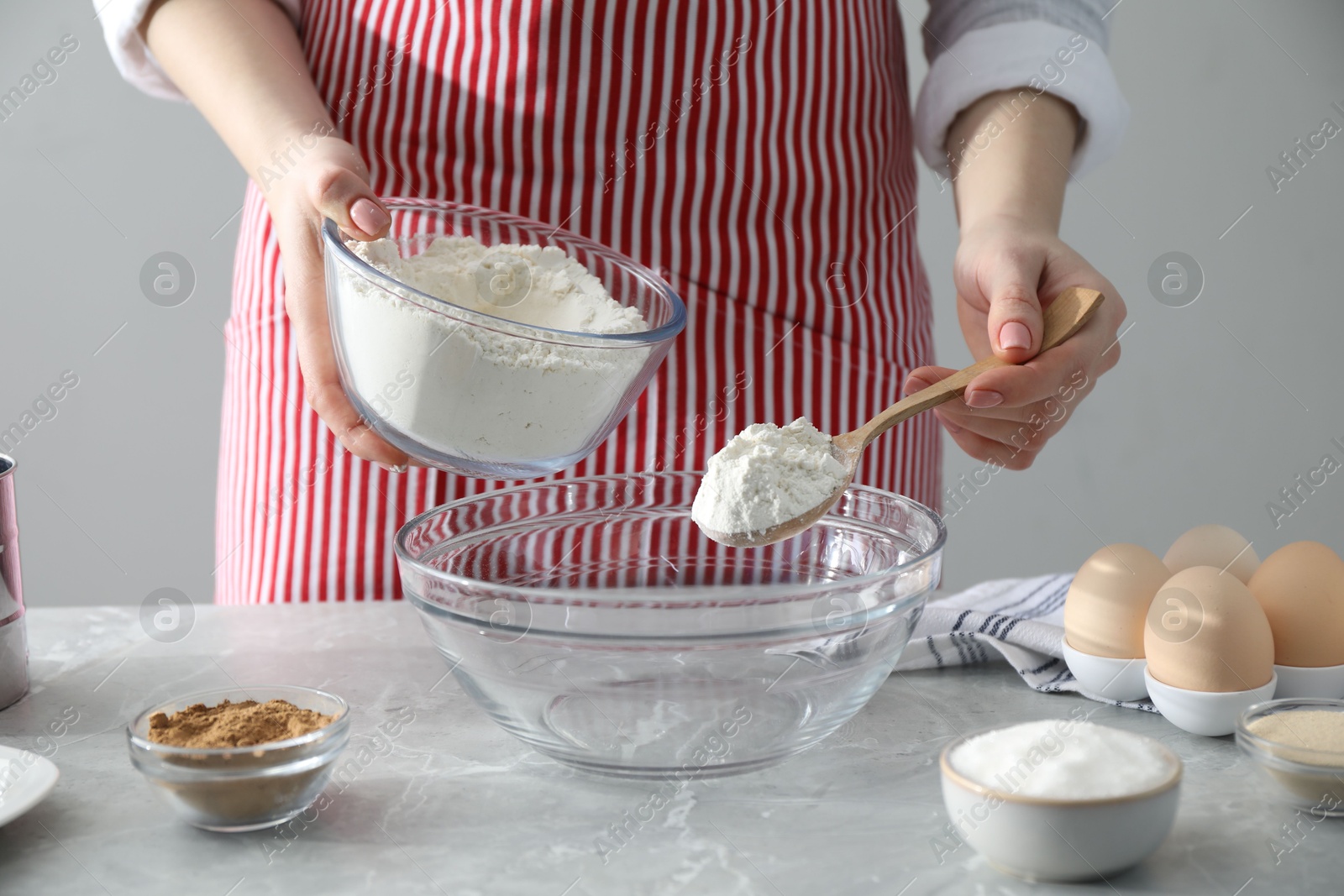 Photo of Making cinnamon rolls. Woman adding flour into bowl at gray marble table, closeup