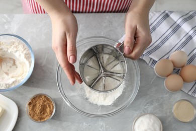 Photo of Making cinnamon rolls. Woman sieving flour at gray marble table, top view