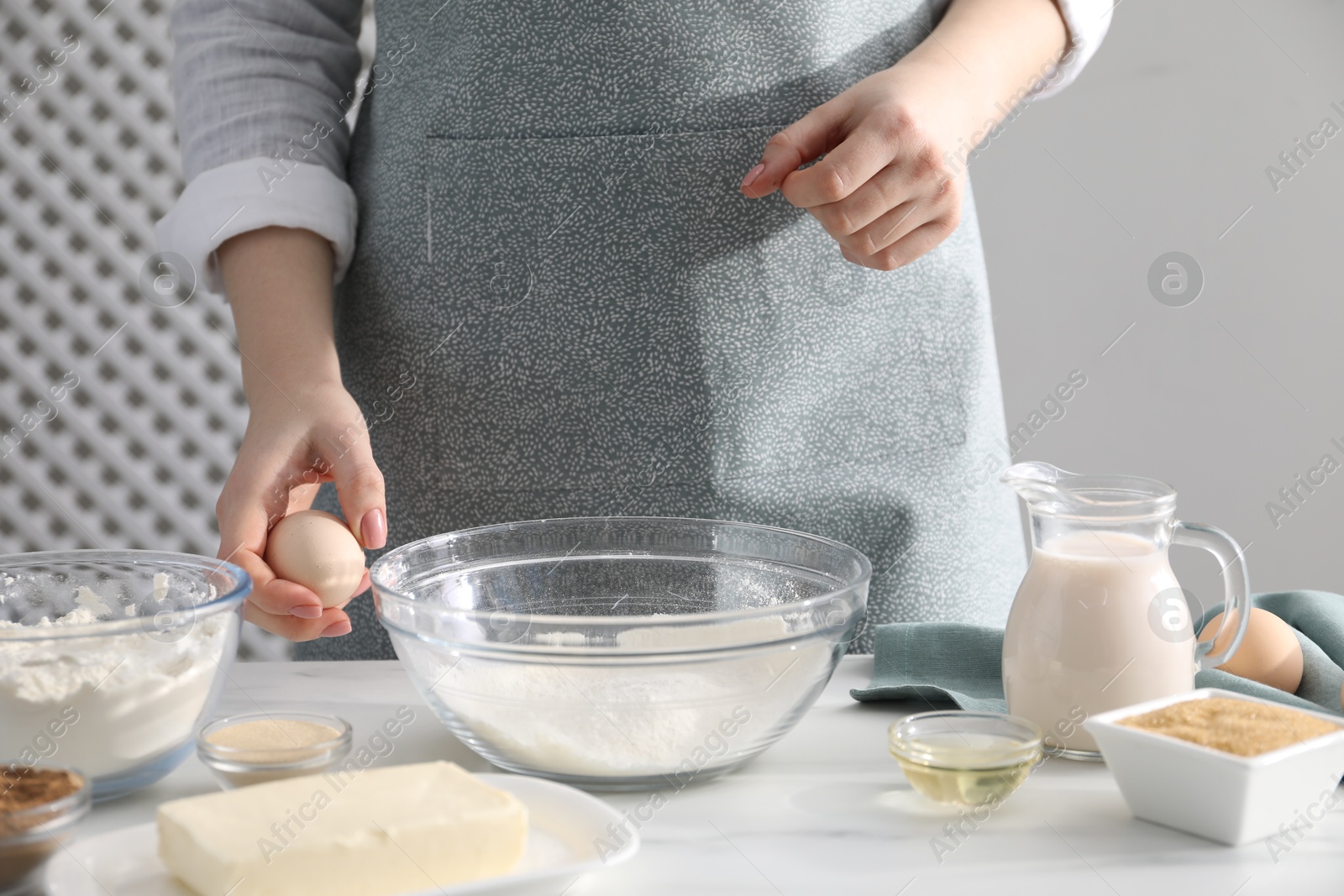 Photo of Making cinnamon rolls. Woman adding egg into bowl at white marble table, closeup