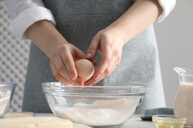 Photo of Making cinnamon rolls. Woman adding egg into bowl at table, closeup