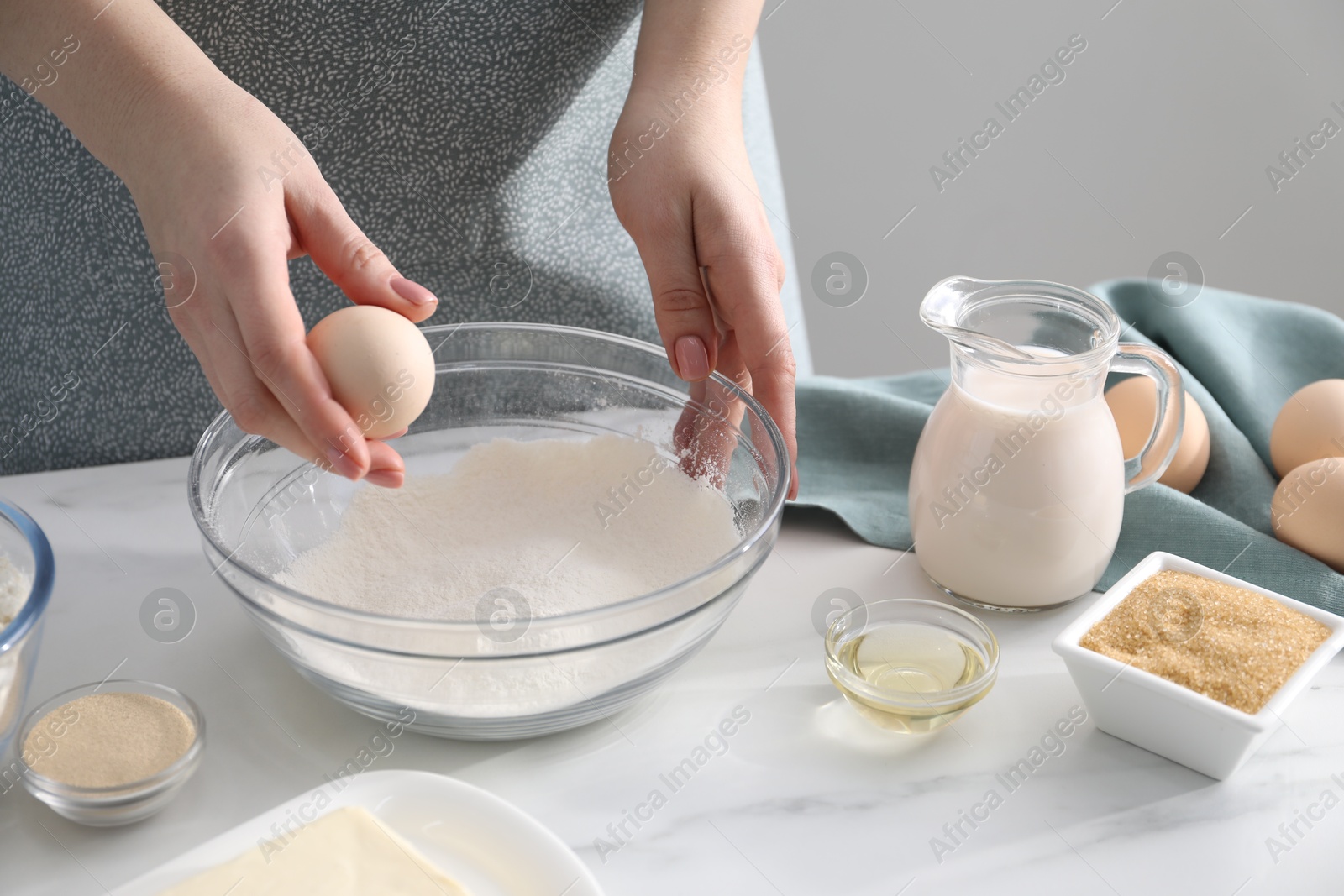 Photo of Making cinnamon rolls. Woman adding egg into bowl at white marble table, closeup