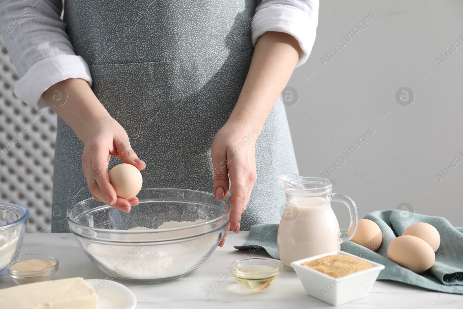 Photo of Making cinnamon rolls. Woman adding egg into bowl at white marble table, closeup