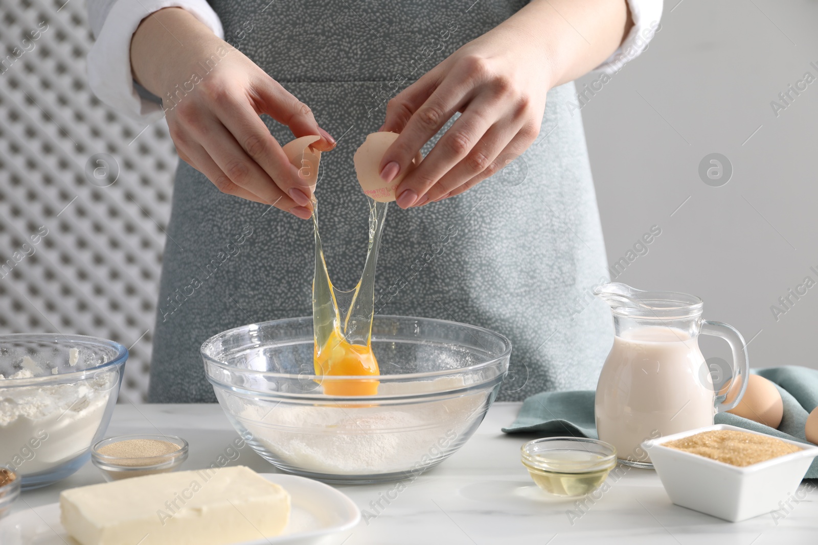 Photo of Making cinnamon rolls. Woman adding egg into bowl at white marble table, closeup