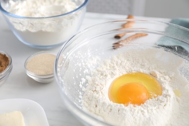 Photo of Making cinnamon rolls. Flour with egg yolk in bowl and other ingredients for dough on white table, closeup