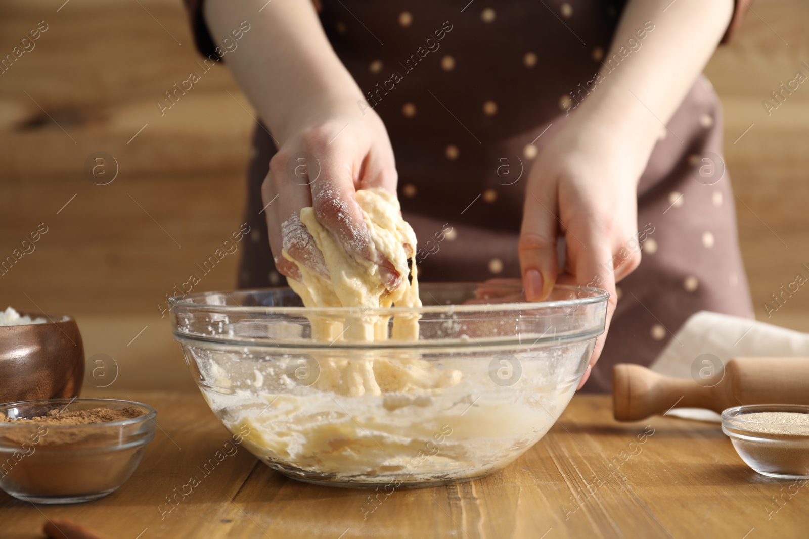 Photo of Woman kneading dough for cinnamon rolls at wooden table, closeup