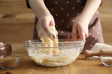 Photo of Woman kneading dough for cinnamon rolls at wooden table, closeup