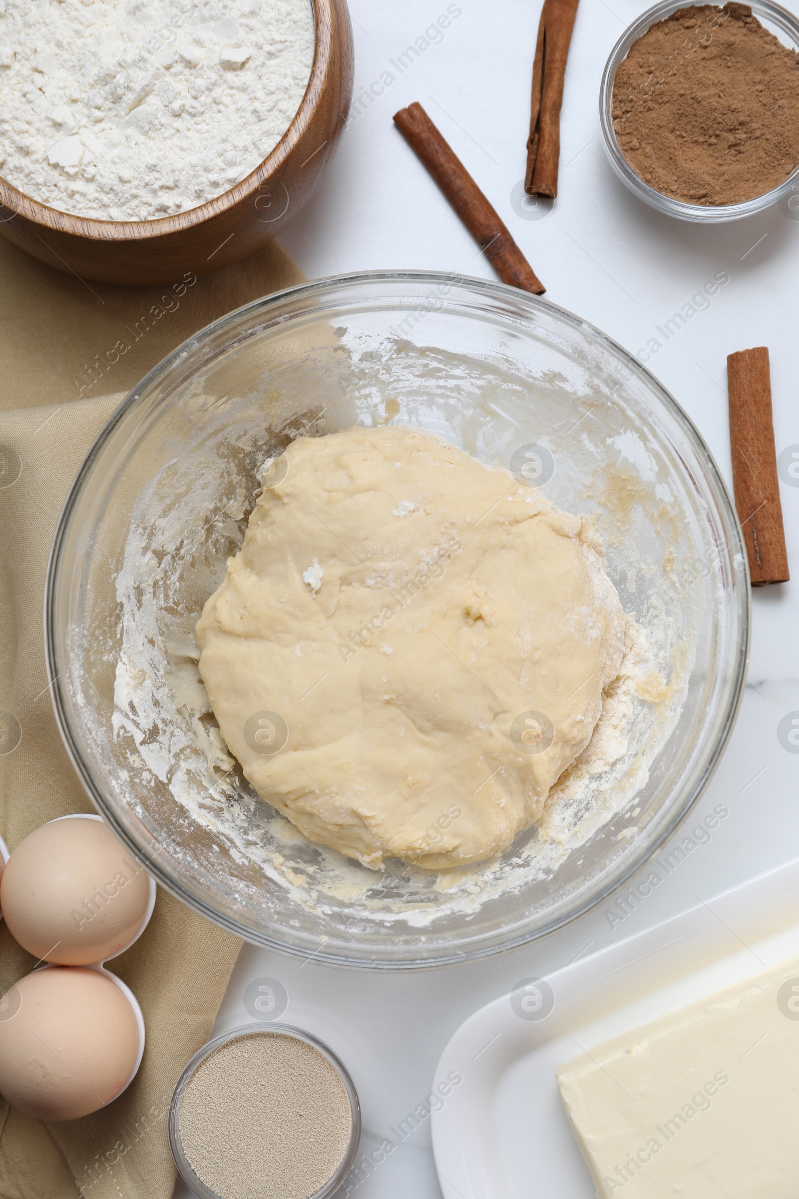 Photo of Making cinnamon rolls. Fresh dough in bowl and ingredients on white table, flat lay