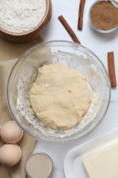 Photo of Making cinnamon rolls. Fresh dough in bowl and ingredients on white table, flat lay