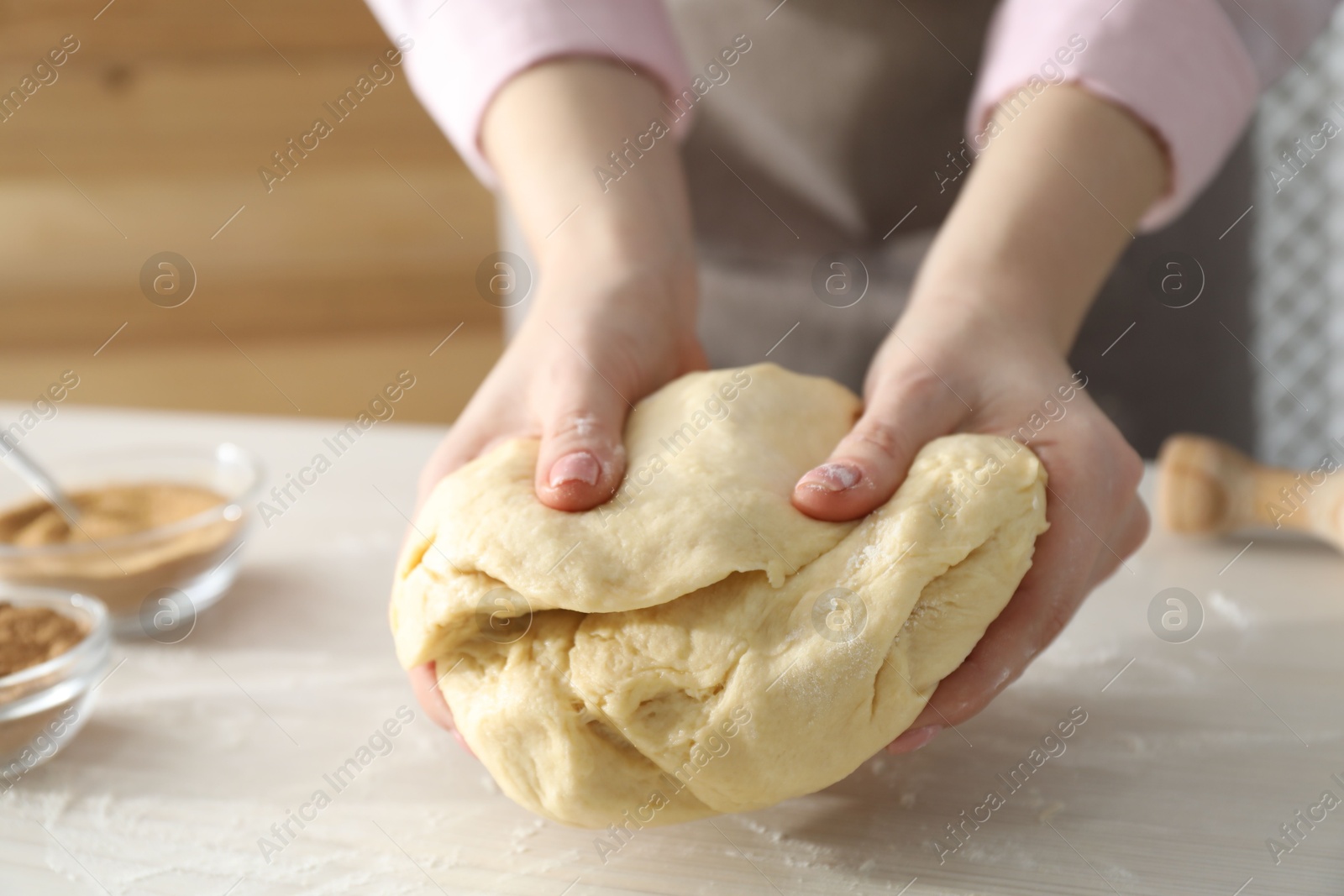 Photo of Woman kneading dough for cinnamon rolls at white table, closeup