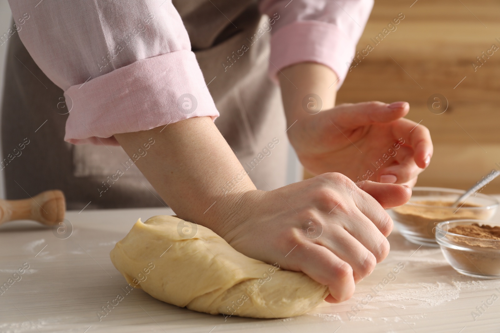 Photo of Woman kneading dough for cinnamon rolls at white wooden table, closeup