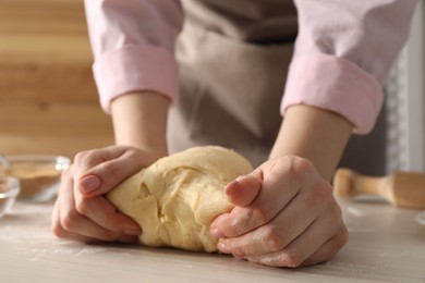 Photo of Woman kneading dough for cinnamon rolls at white wooden table, closeup