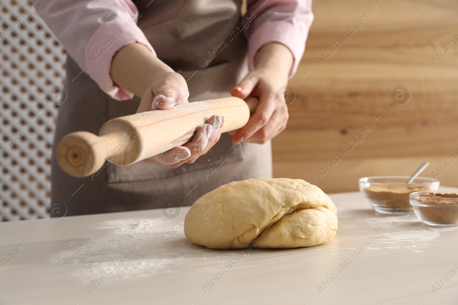 Photo of Making cinnamon rolls. Woman with rolling pin and dough at white wooden table, closeup