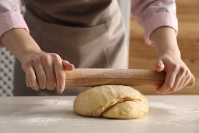 Photo of Making cinnamon rolls. Woman shaping dough with rolling pin at white wooden table, closeup