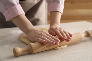 Making cinnamon rolls. Woman shaping dough with rolling pin at white wooden table, closeup