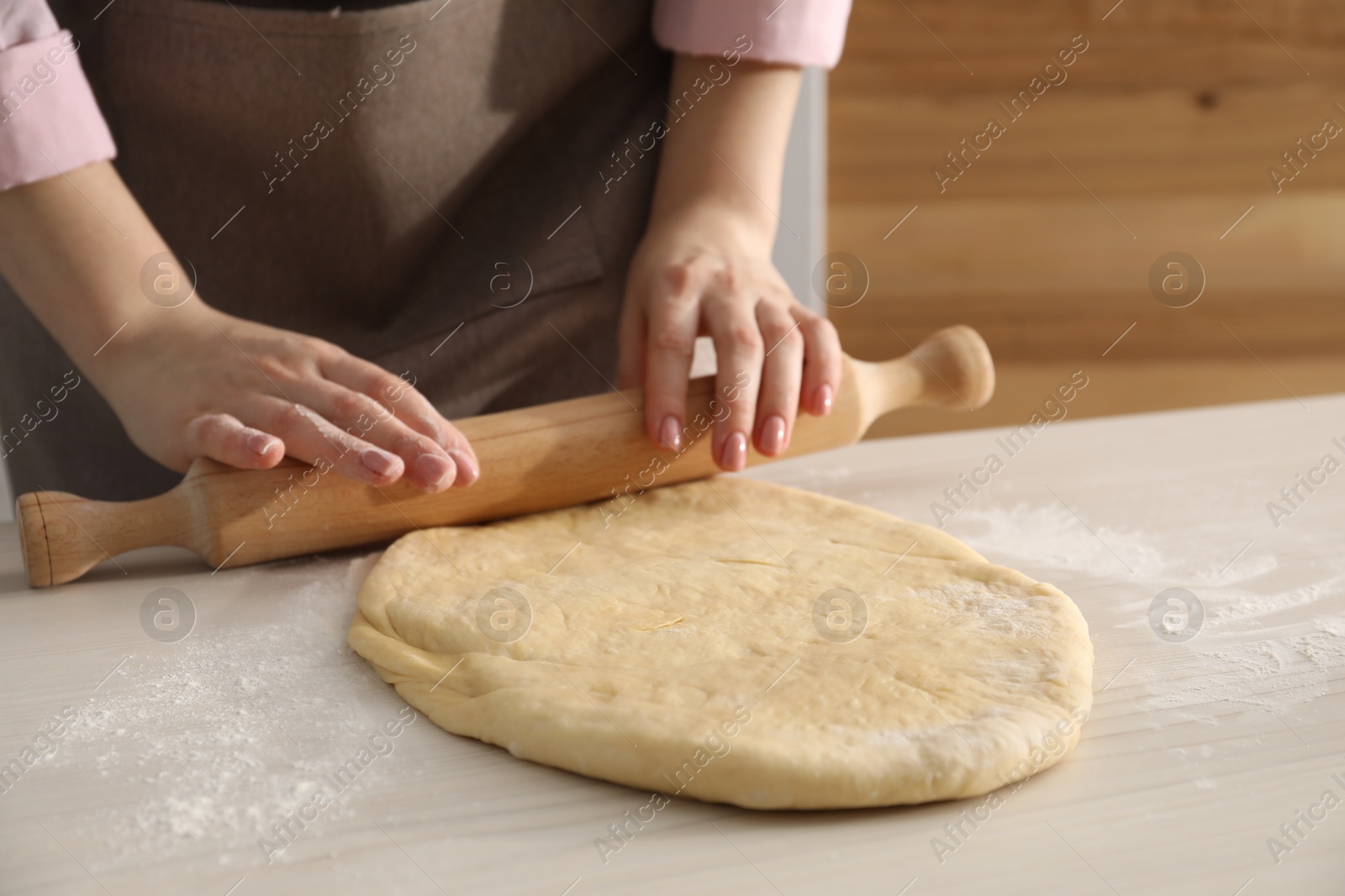 Photo of Making cinnamon rolls. Woman shaping dough with rolling pin at white wooden table, closeup