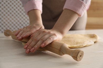 Photo of Making cinnamon rolls. Woman shaping dough with rolling pin at white wooden table, closeup