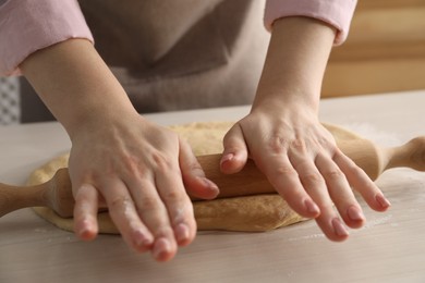 Photo of Making cinnamon rolls. Woman shaping dough with rolling pin at white wooden table, closeup