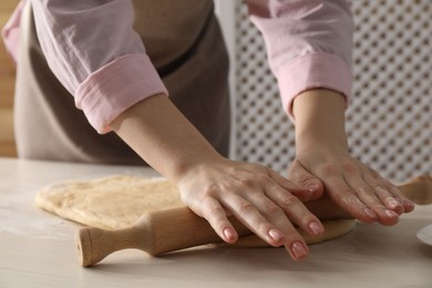 Photo of Making cinnamon rolls. Woman shaping dough with rolling pin at white wooden table, closeup