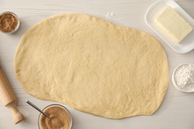 Making cinnamon rolls. Dough, other ingredients and rolling pin on white wooden table, flat lay