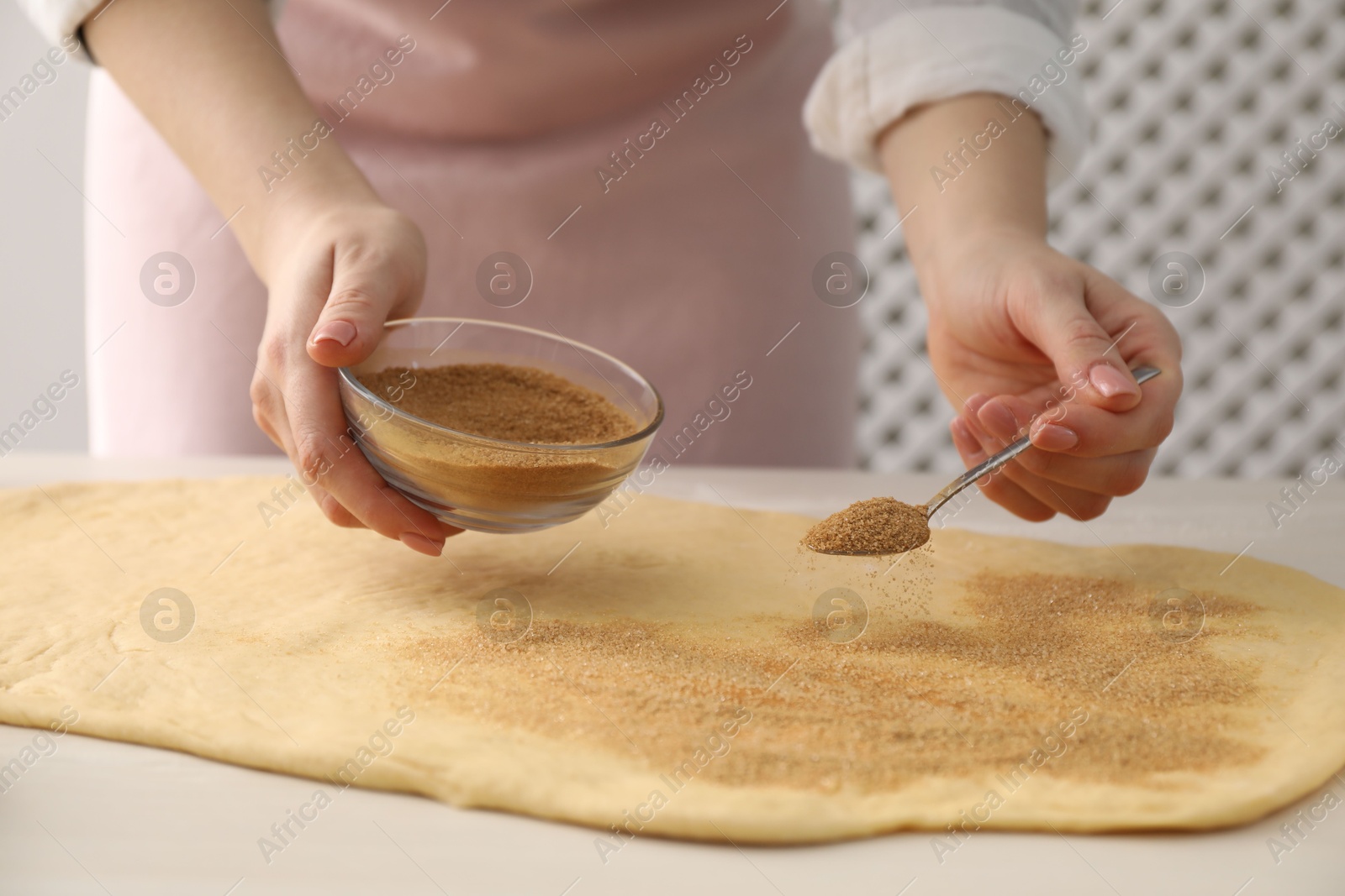 Photo of Making cinnamon rolls. Woman adding spice with sugar into dough at white wooden table, closeup