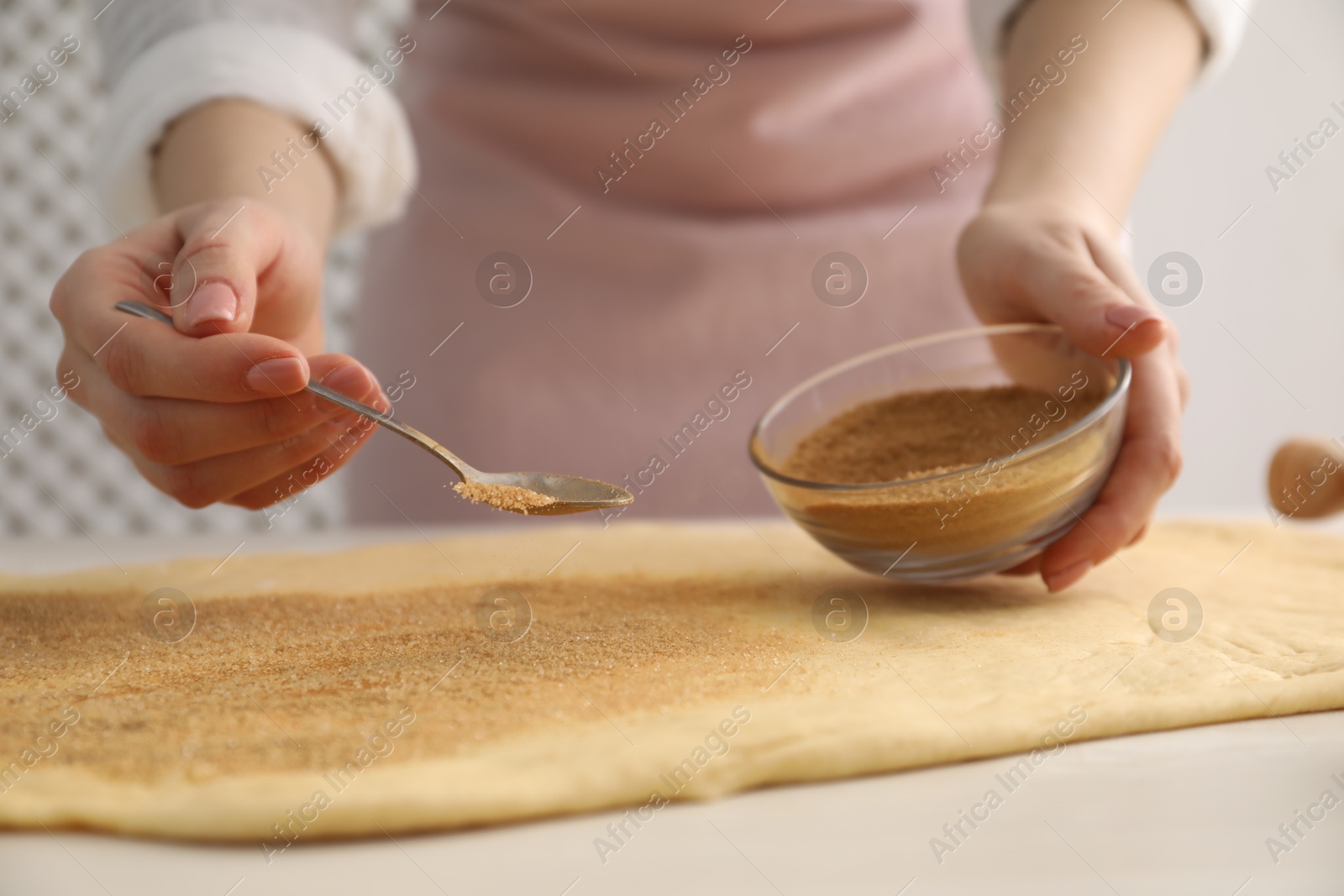 Photo of Making cinnamon rolls. Woman adding spice with sugar into dough at white wooden table, closeup