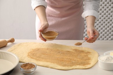 Photo of Making cinnamon rolls. Woman adding spice with sugar into dough at white wooden table, closeup